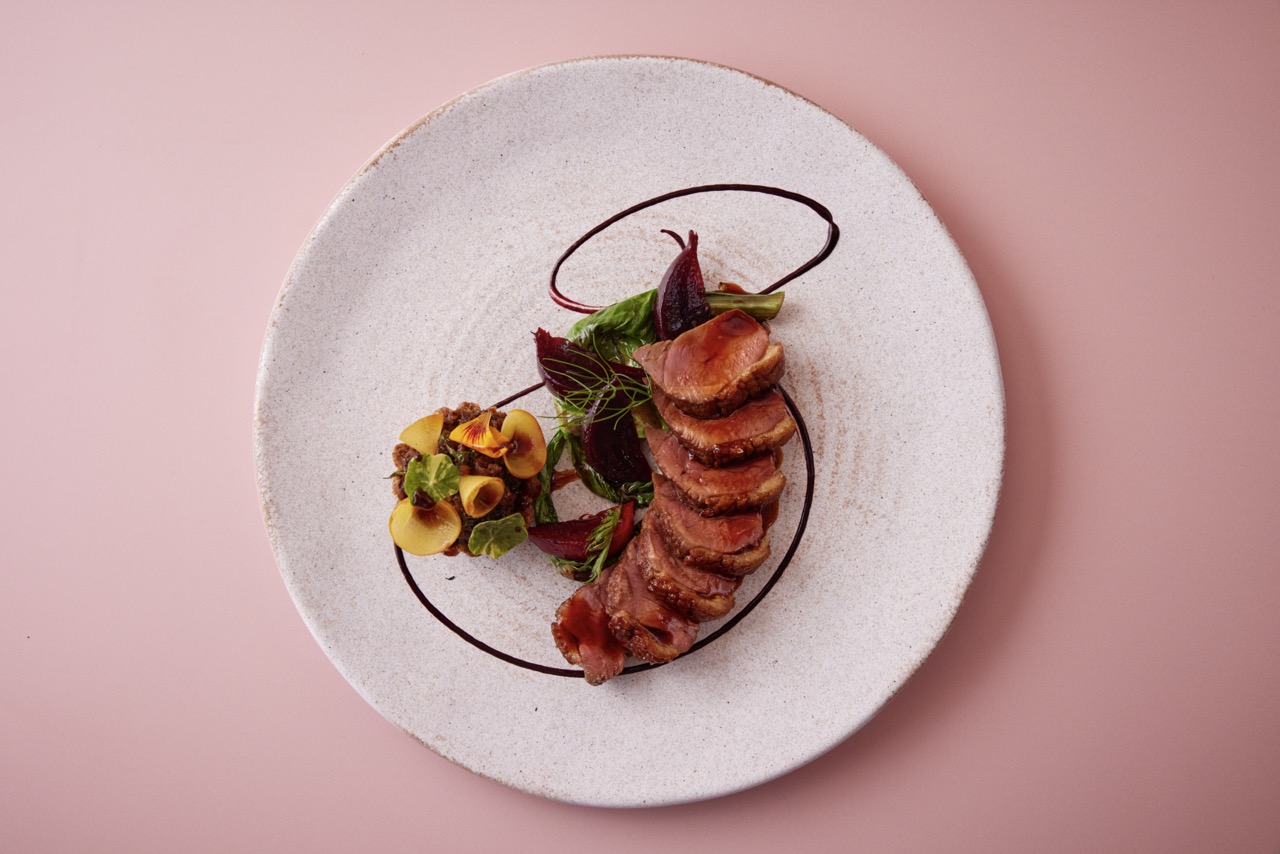 Overhead shot of beautiful duck dish at Apricity, on white plate against pink surface