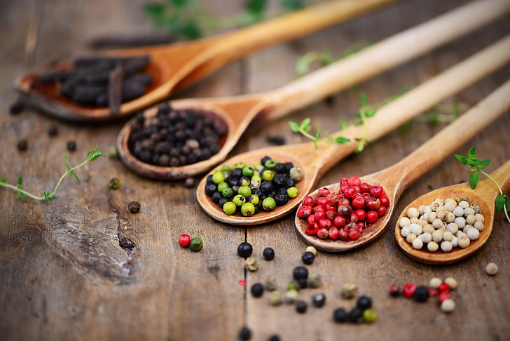 Different coloured spices on five wooden spoons