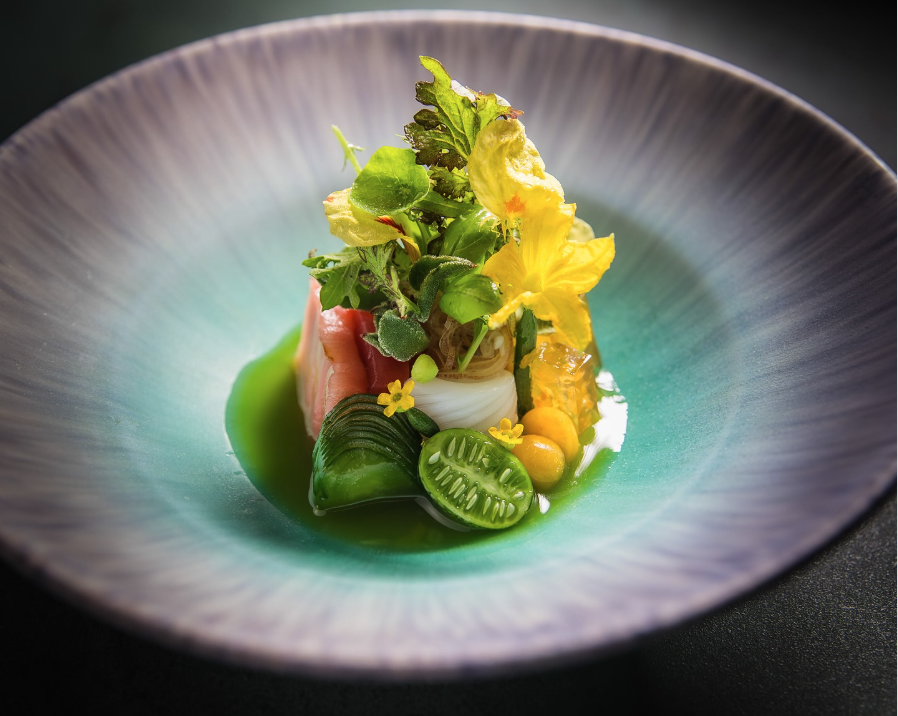 A close-up of a colourful fine dining fish dish with green tomatoes and edible flowers, arranged in a beautiful bowl