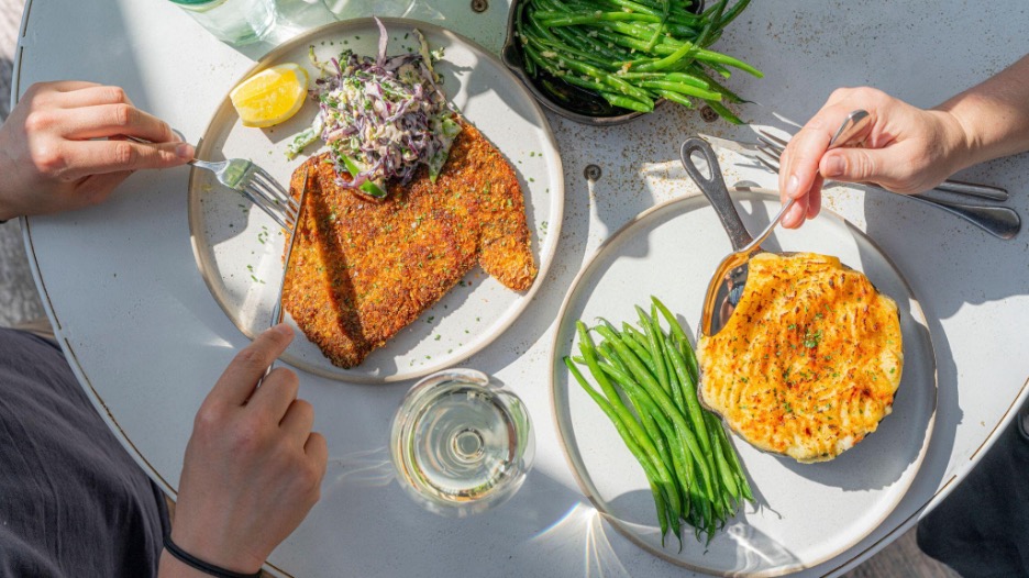 Overhead shot of people eating chicken schnitzel, potato gratin and green beans