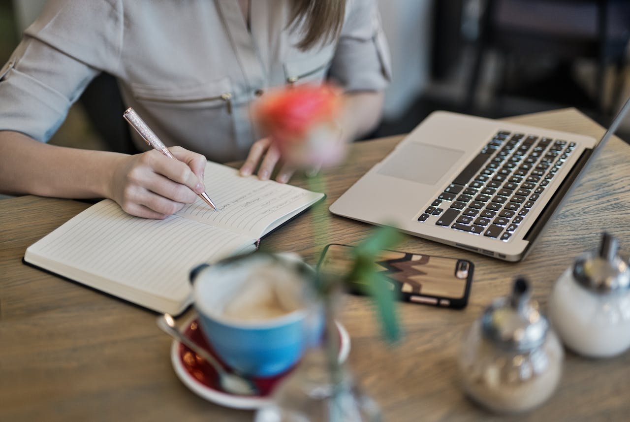 Woman taking notes from laptop in a café setting, with a coffee beside her on the table