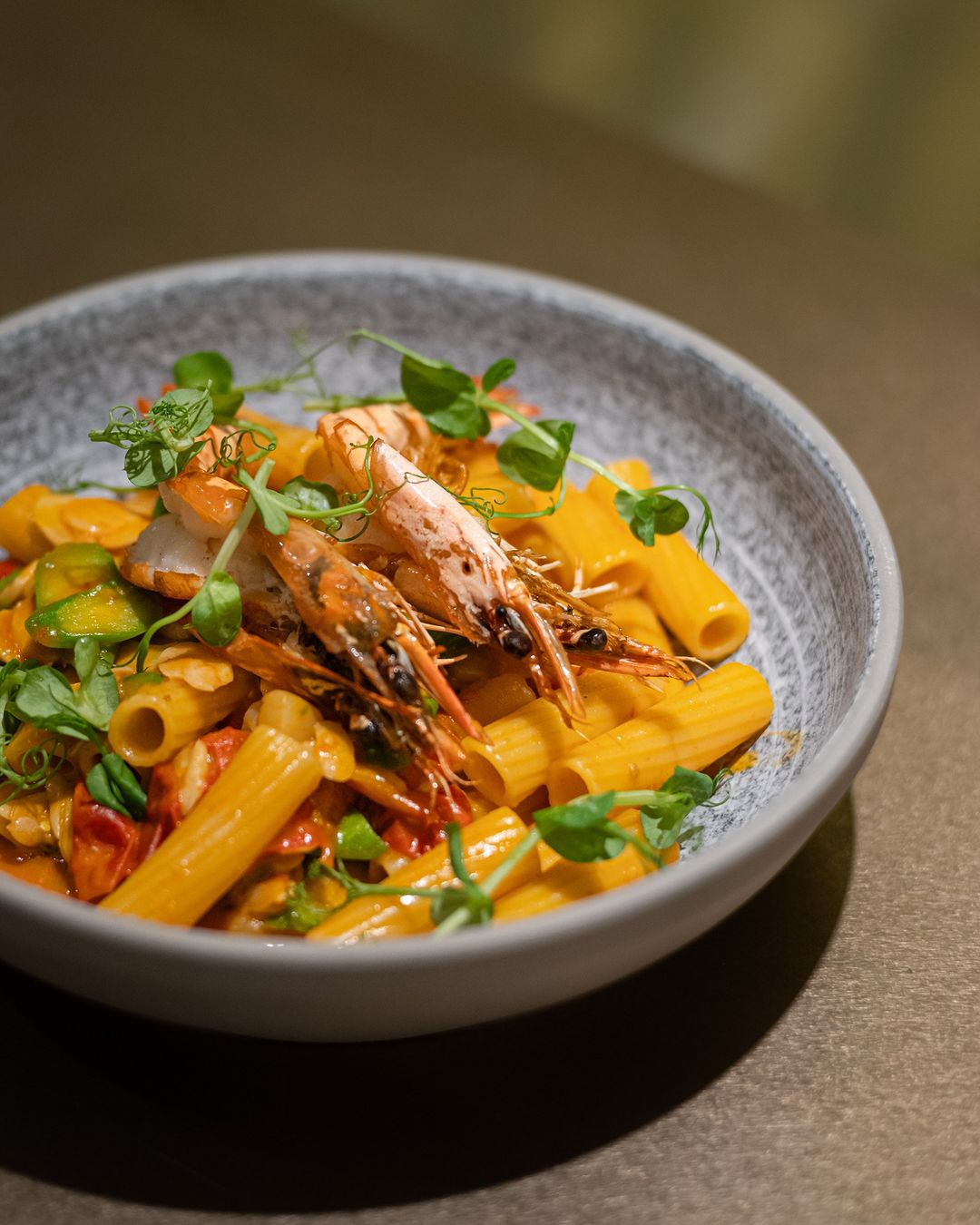 Grey bowl of pasta topped with prawns in the shell