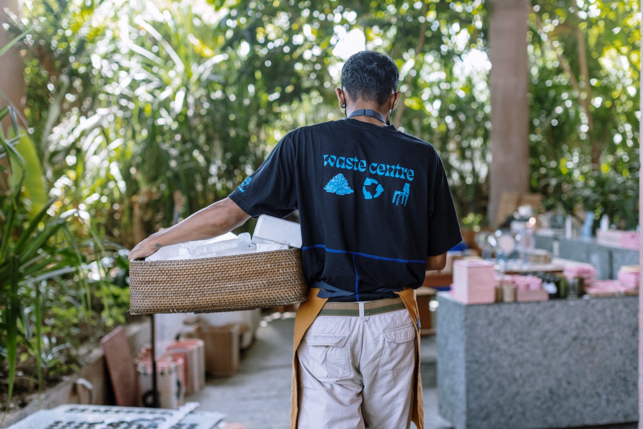 A worker walking with his back to the camera, wearing a t-shirt that says Waste Centre and carrying a basket