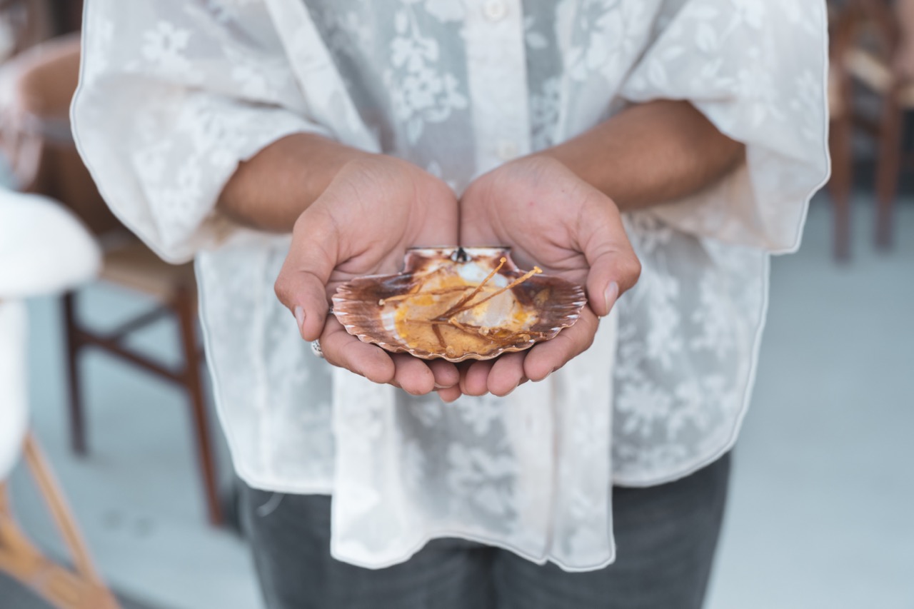 Hands holding a scallop shell filled with a seared scallop