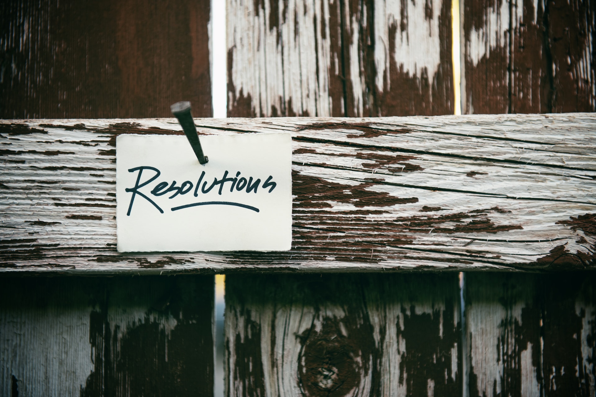 Black and white photo of piece of paper saying 'resolutions' pinned to wooden fence