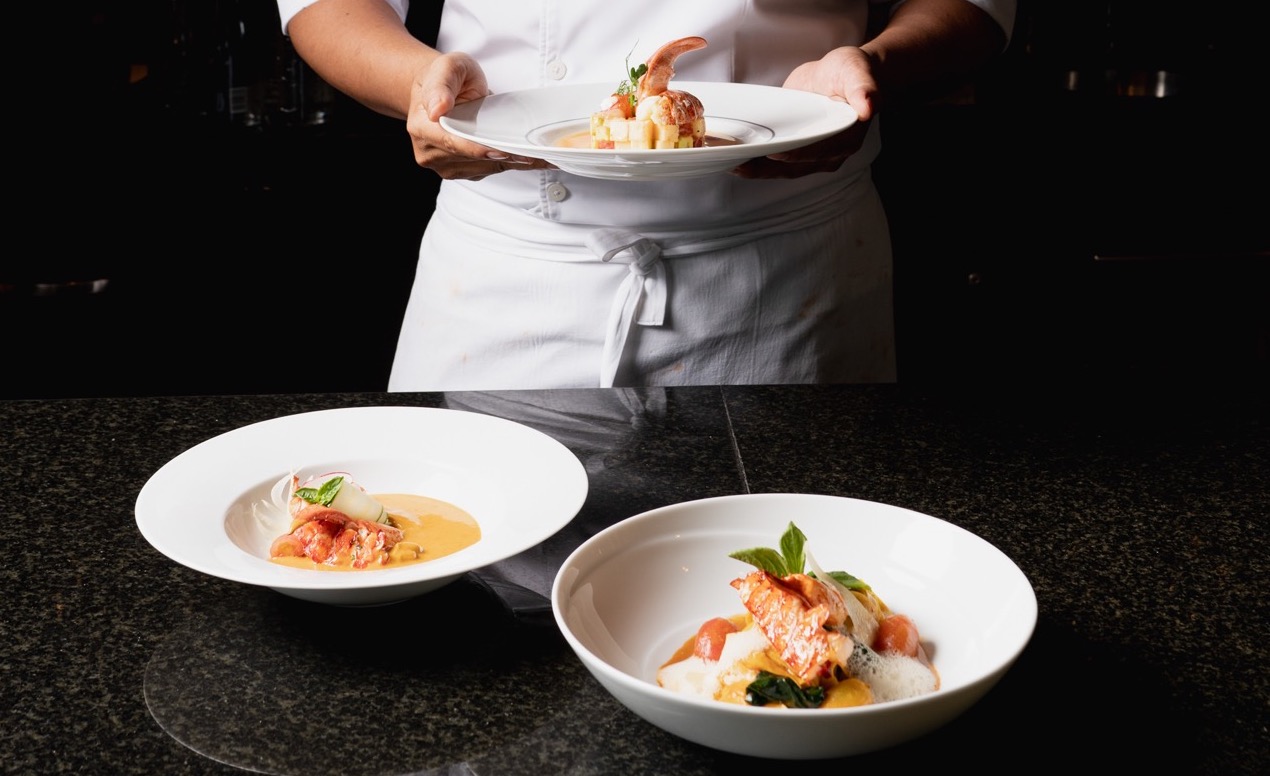 A chef with three white bowls of food all against a black background