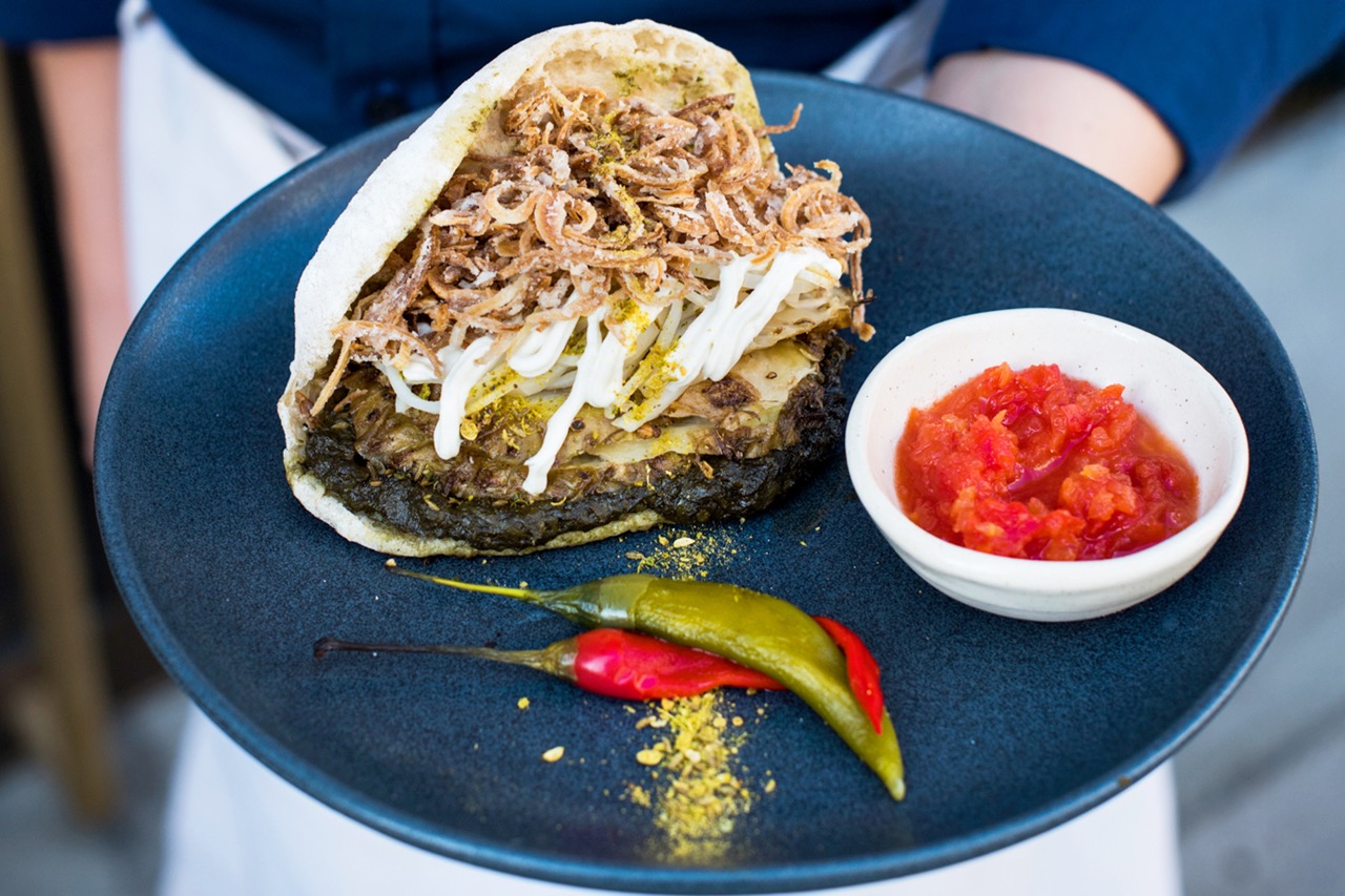 Chef in apron holding celeriac shawarma dish at ROVI by Ottolenghi