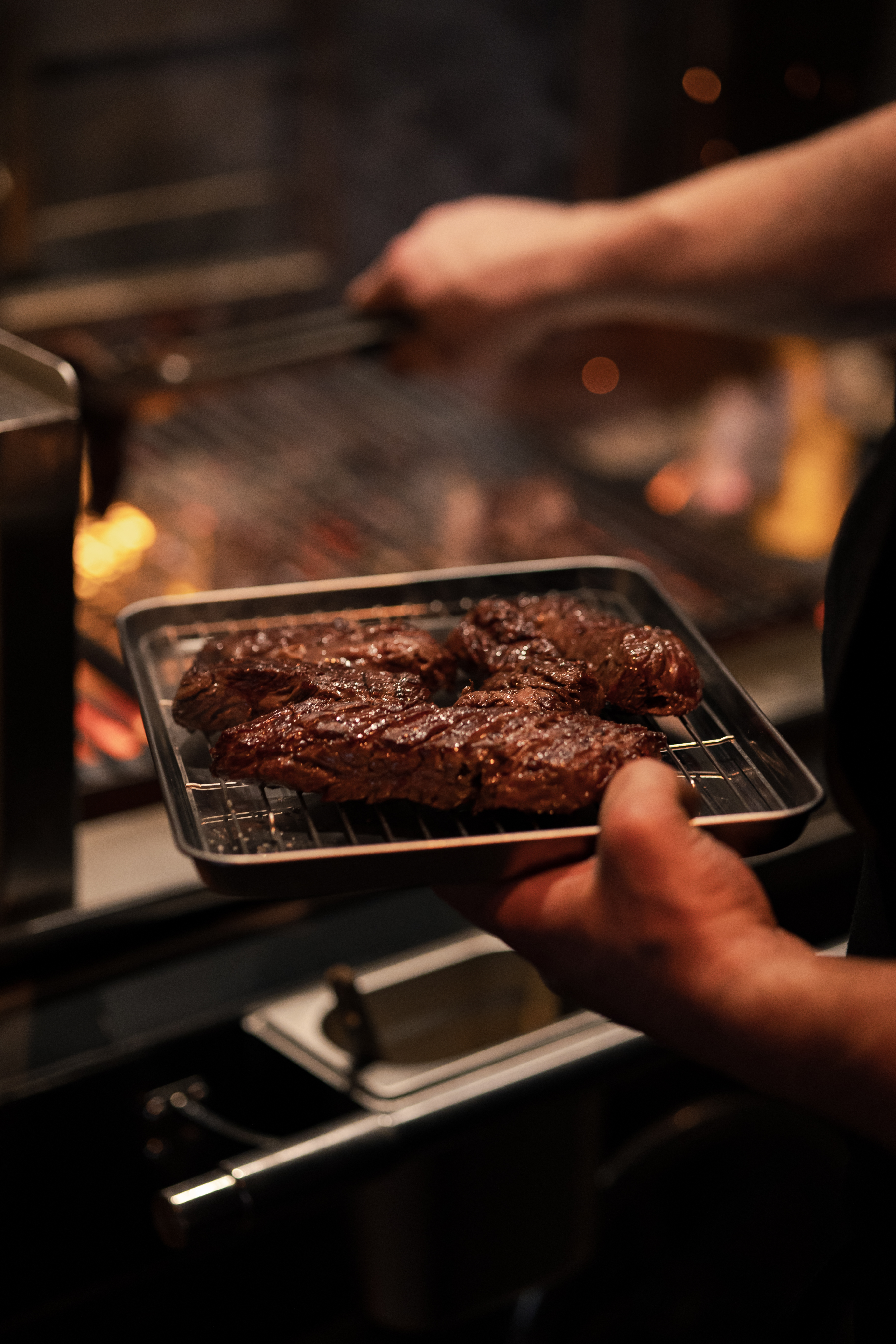 Hand holding small pan with steaks on top of a rack