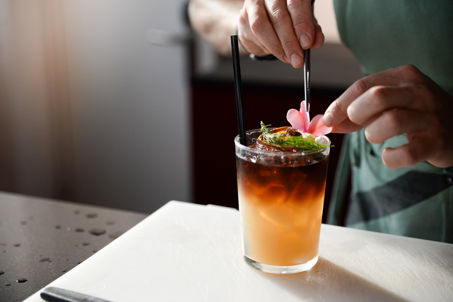 Bartender adding final touch to duo-tone cocktail with pink edible flower