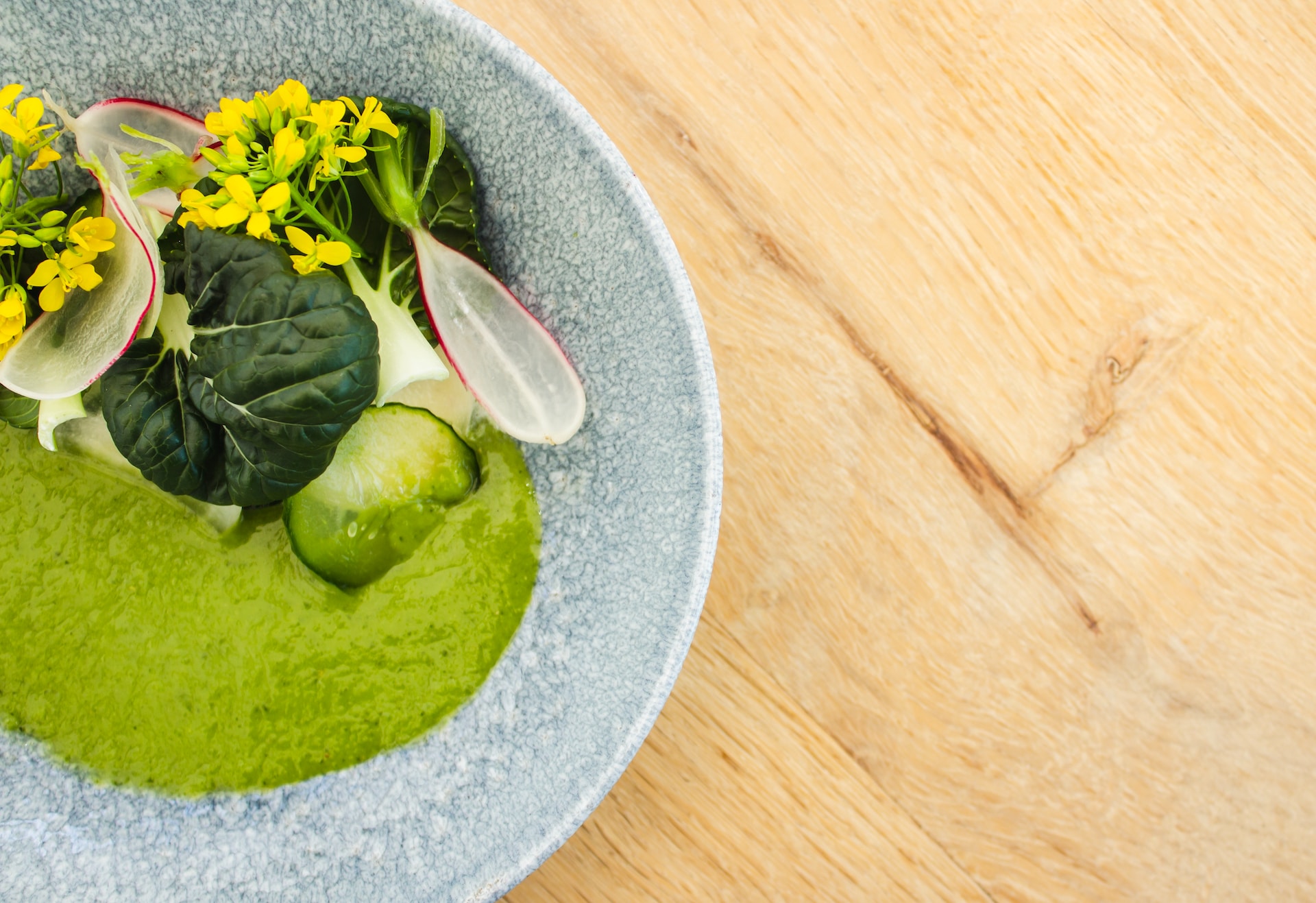 Fancy salad with edible flowers and green purée in grey bowl on wooden table