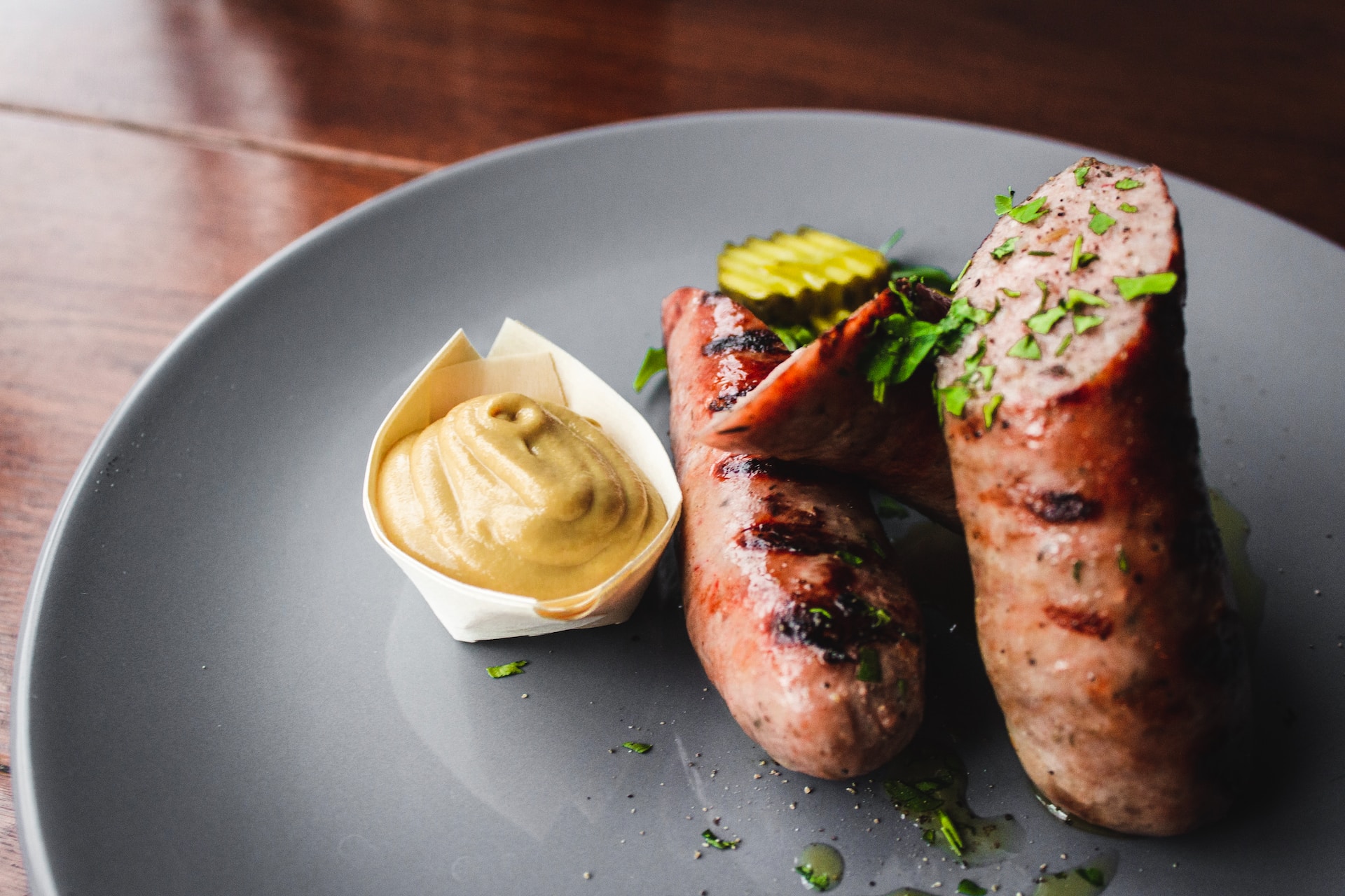 Halved sausage on dark plate with pickles and mustard