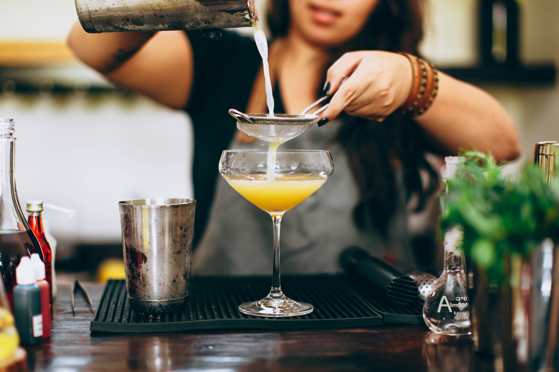 Bartender straining cocktail shaker through sieve into coupe glass