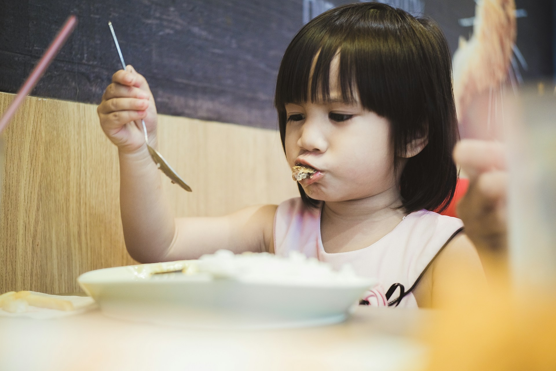 Little girl eating bowl of food with spoon