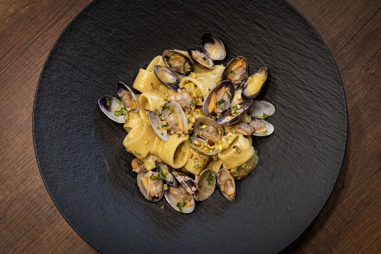Overhead shot of clam pasta dish on a black plate against a dark wooden surface