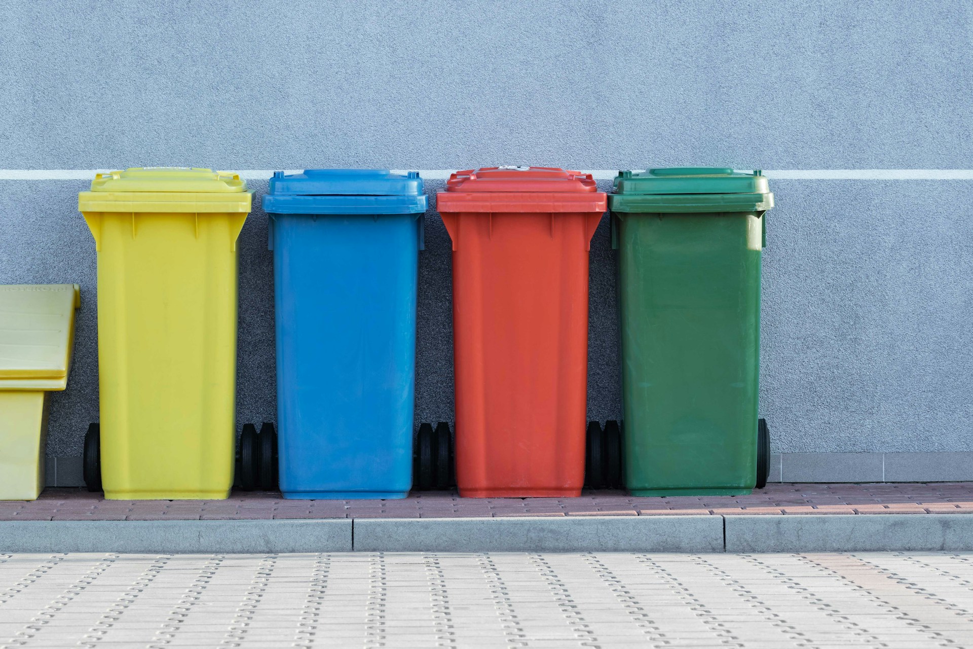 Four bins against an exterior wall, in different colours (yellow, blue, red, green)