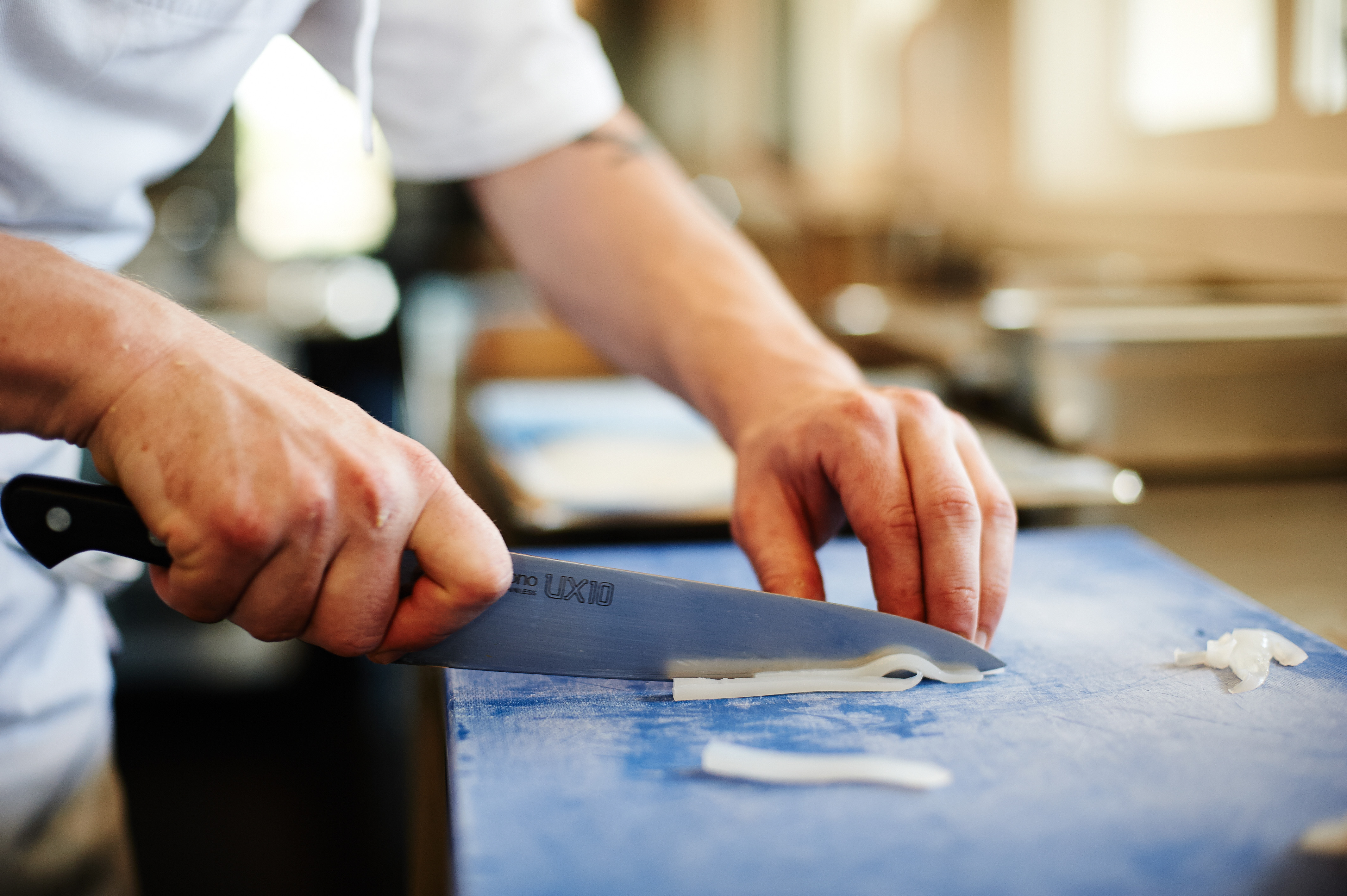 Close up of chef's hands thinly slicing white fish on blue chopping board