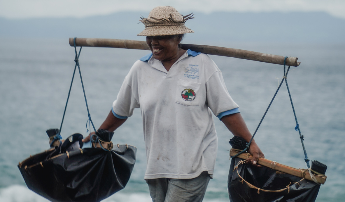 Native Balinese salt producer carrying two buckets of water up from the sea, balanced on bamboo across the shoulders