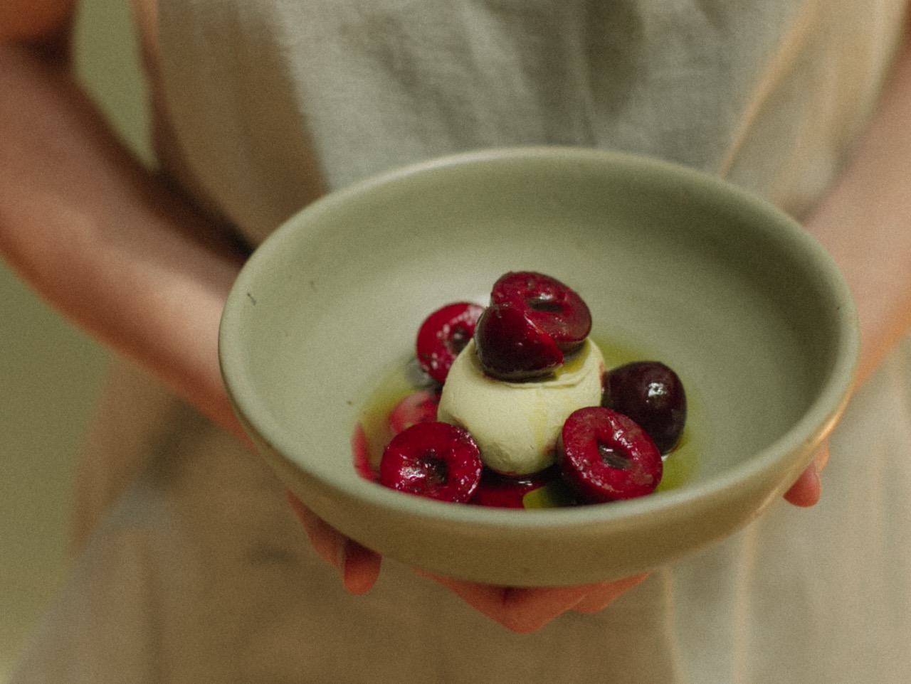 Hands holding pale-coloured bowl of fresh plums with panna cotta