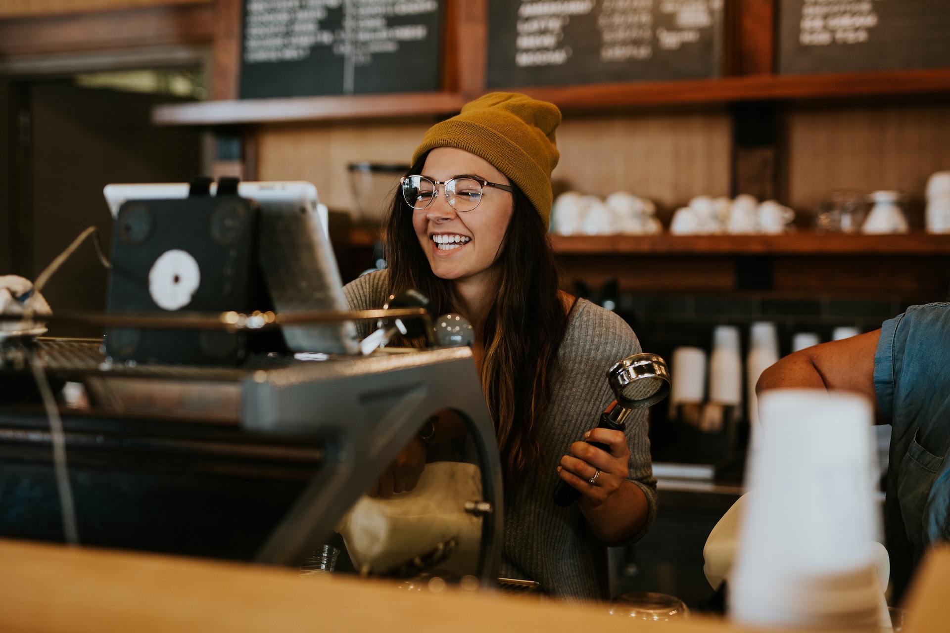 Smiling barista at till wearing a yellow beanie