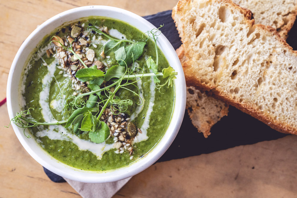 Overhead shot of green soup in bowl and two slices of bread beside it