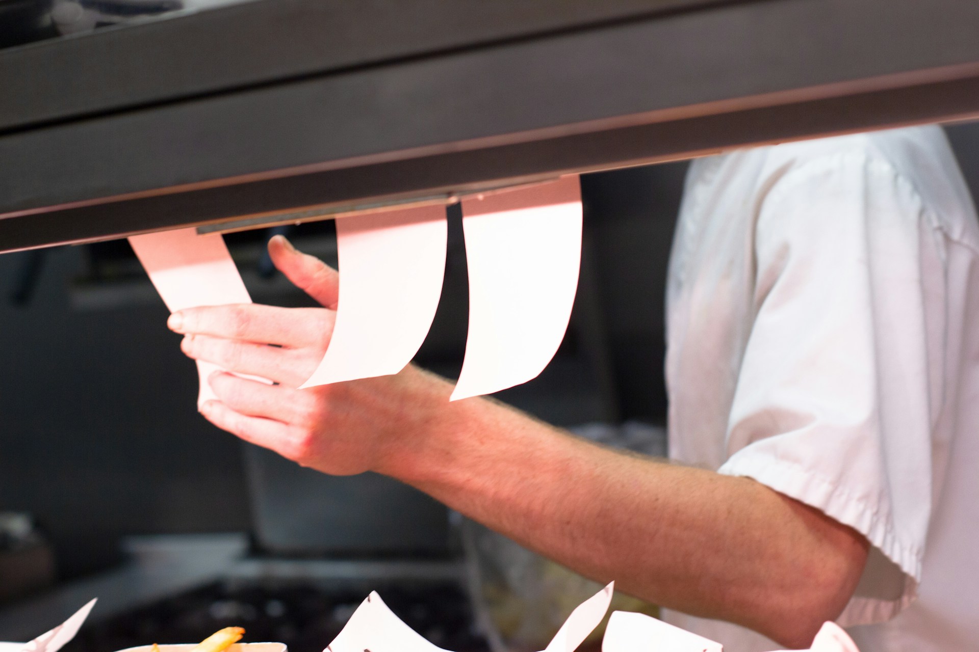 Chef in white jacket looking at orders on the pass