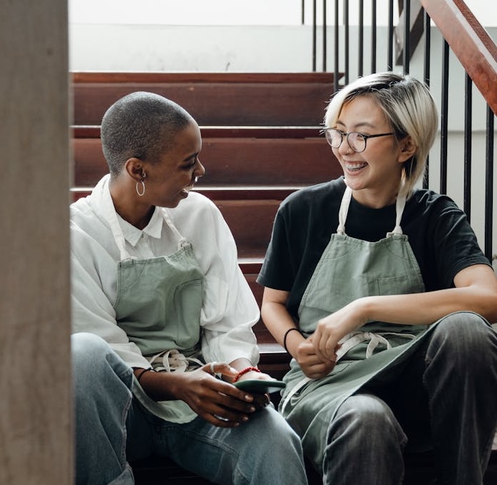 Two restaurant employees in aprons relaxing and chatting on a back staircase