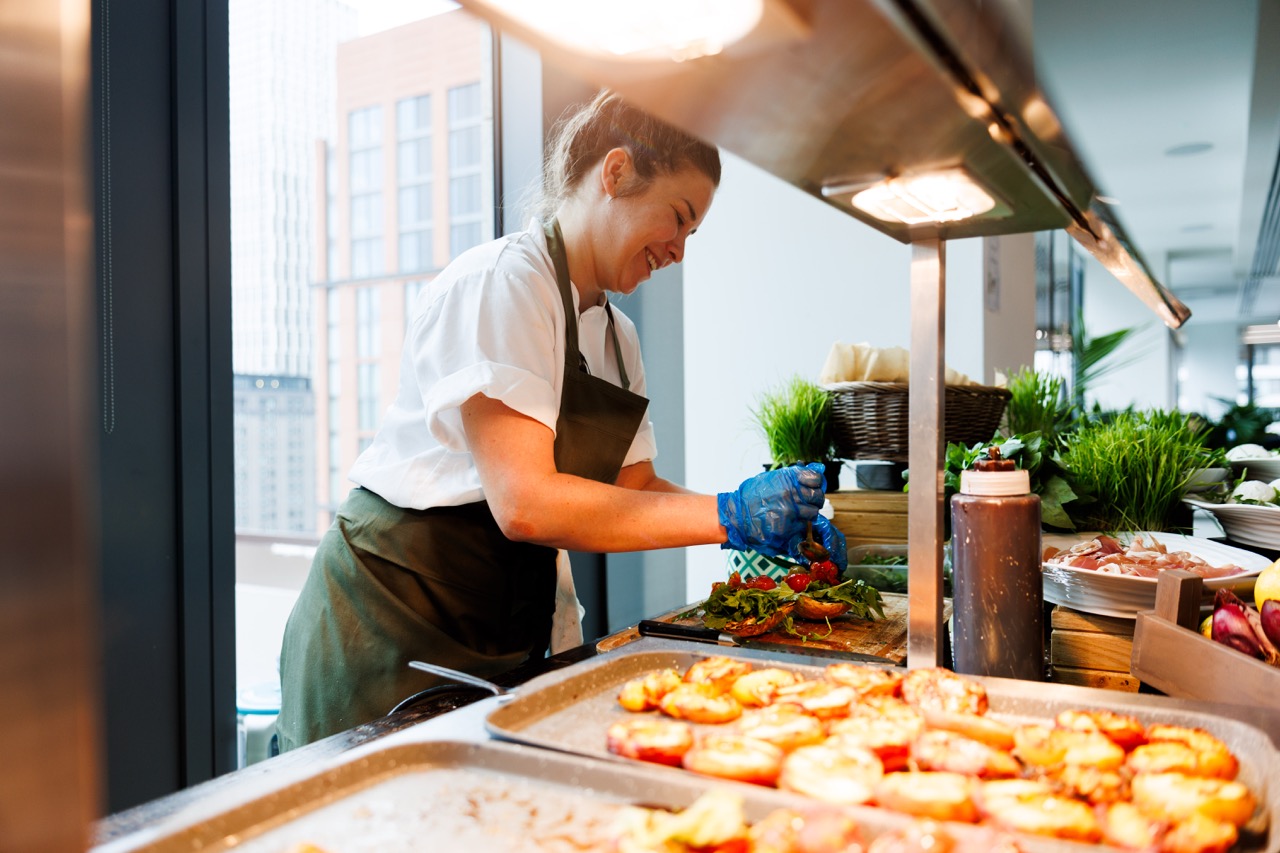 A smiling staff member in a green apron serving food at Genuine Dining