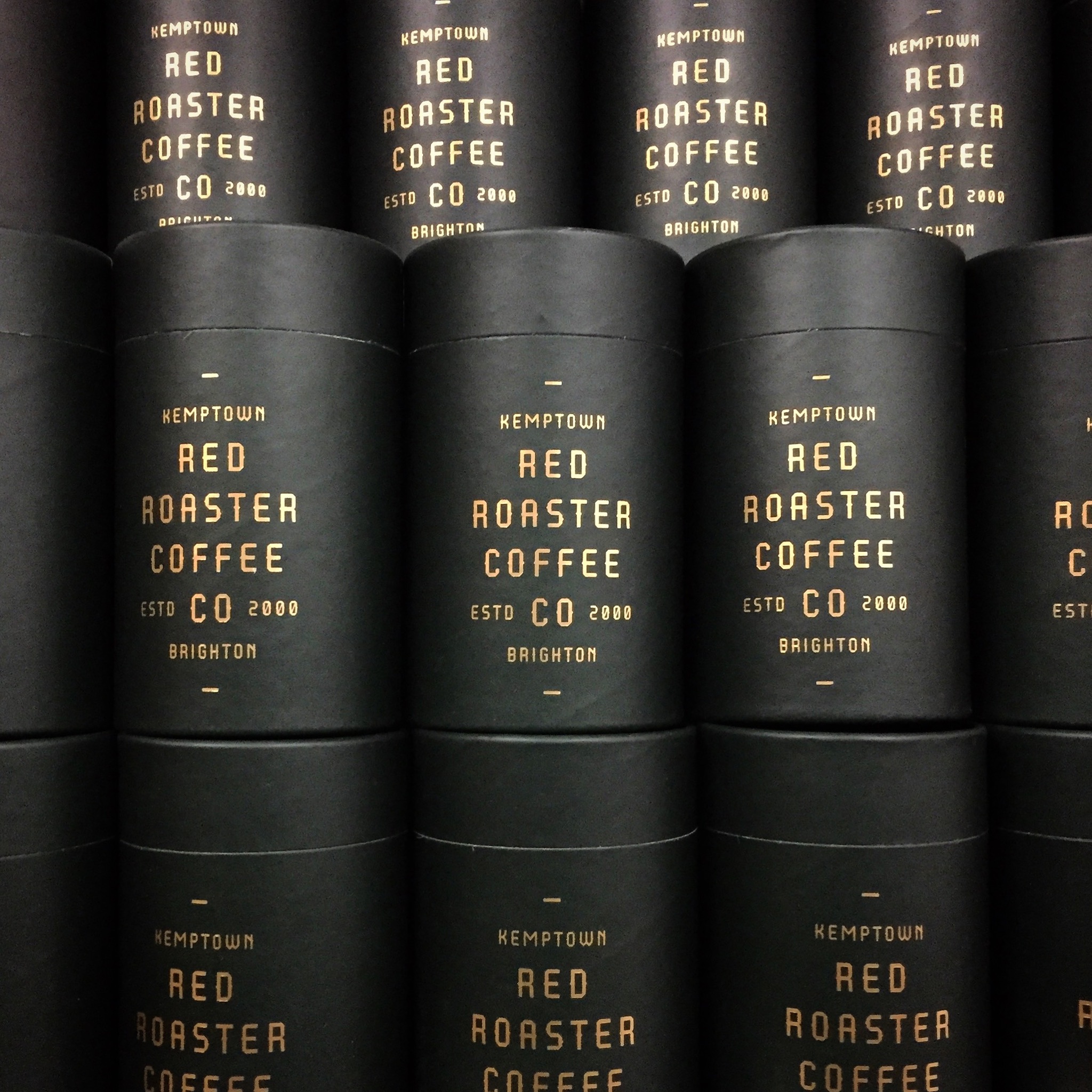 Stacks of black tubs saying Red Roaster Coffee in gold letters