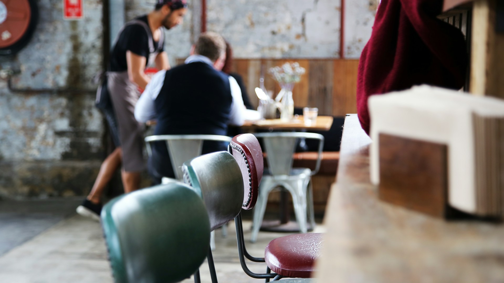 Close up shot of empty seats at table in restaurant with customers and server in the background