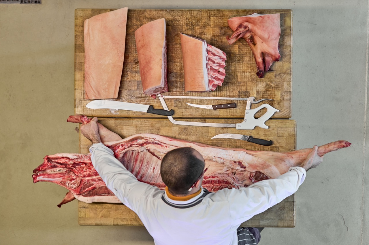 Overhead shot of a butcher at a butcher's block breaking down a whole pig