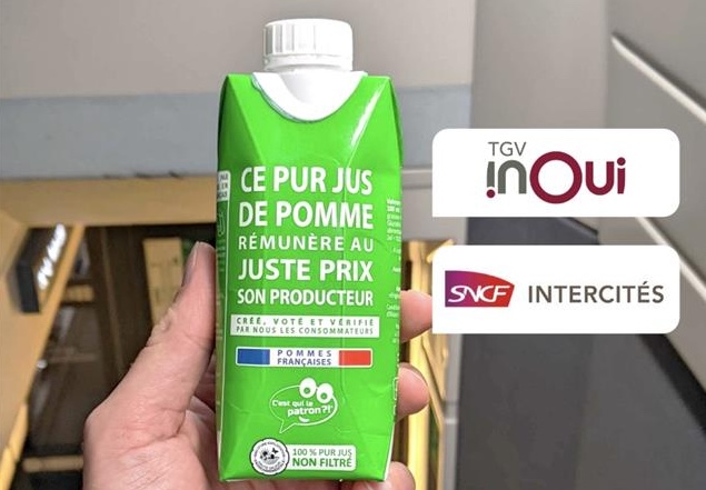 A hand holding a green carton of fresh French apple juice on board a Newrest Wagons Lits train