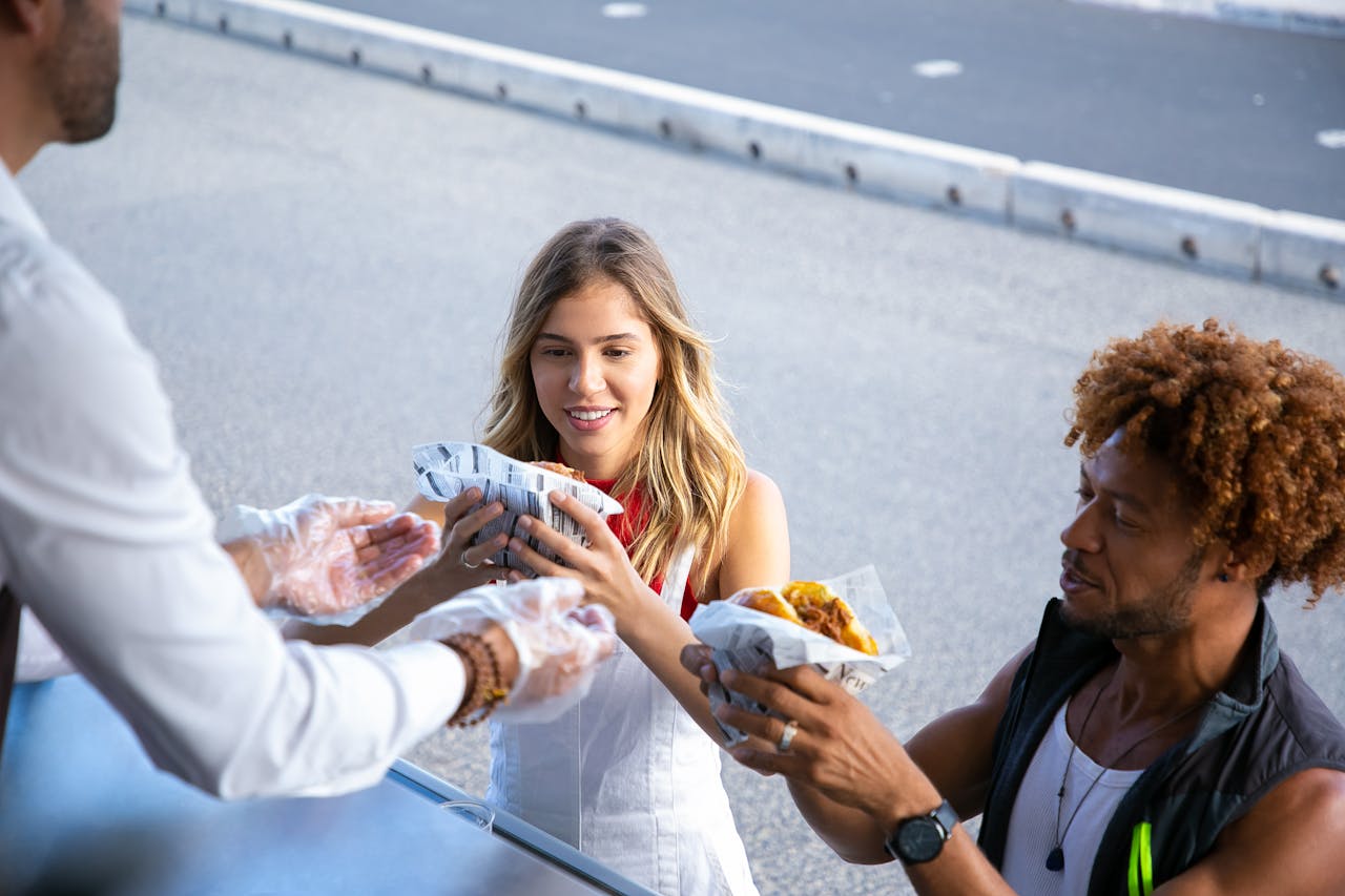 A woman and a man taking street food wrapped in paper from a vendor in a food truck