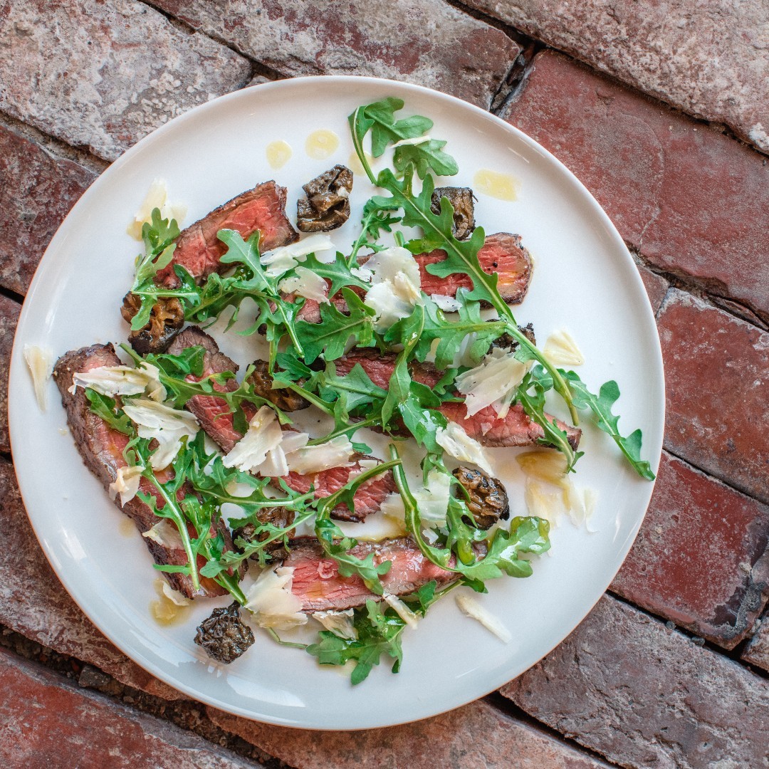 Overhead shot of sliced rare beef, Parmesan and rocket on white plate at Roth Bar & Grill