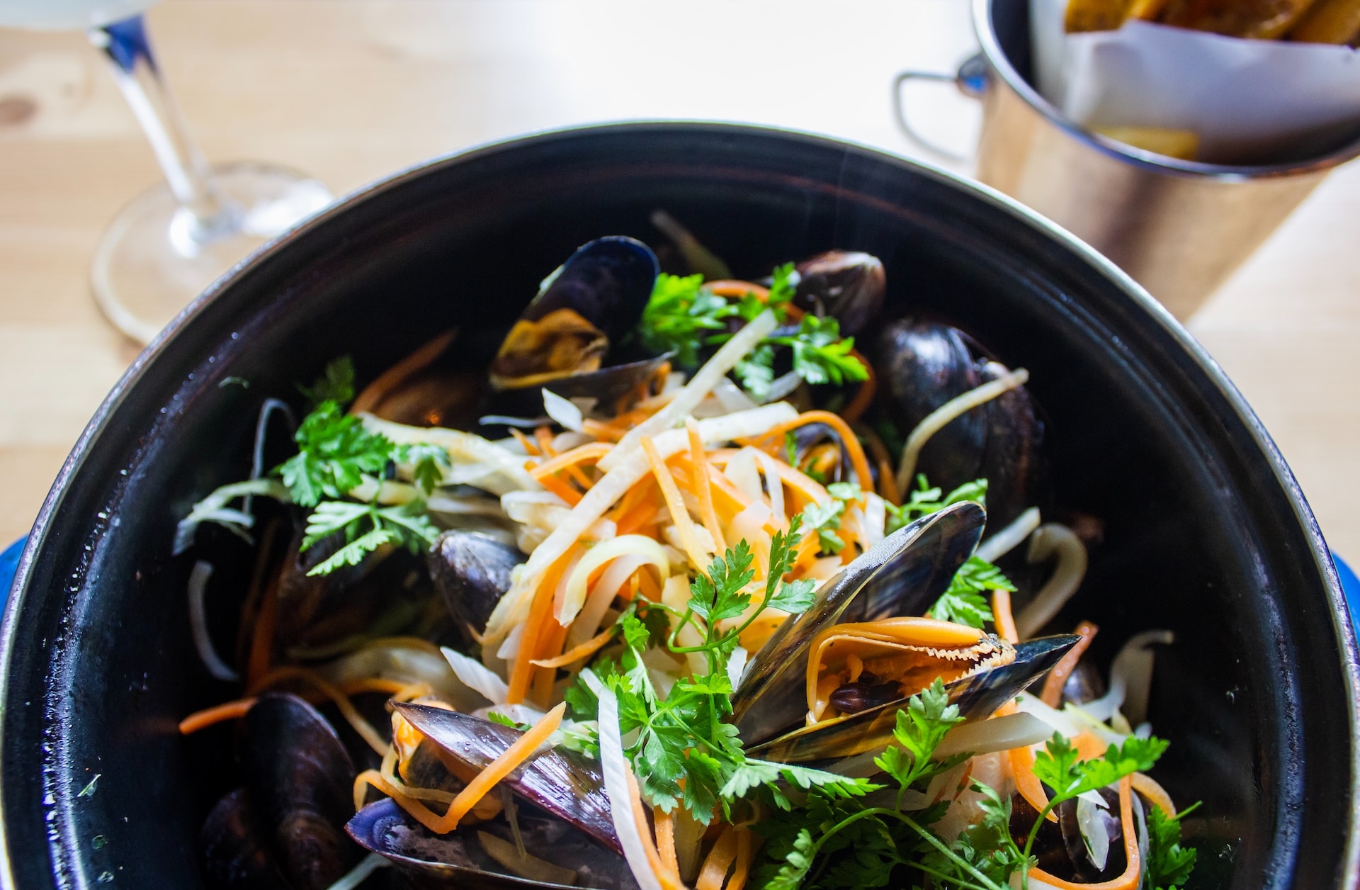 Black pot of cooked mussels with parsley, bean sprouts and grated carrot
