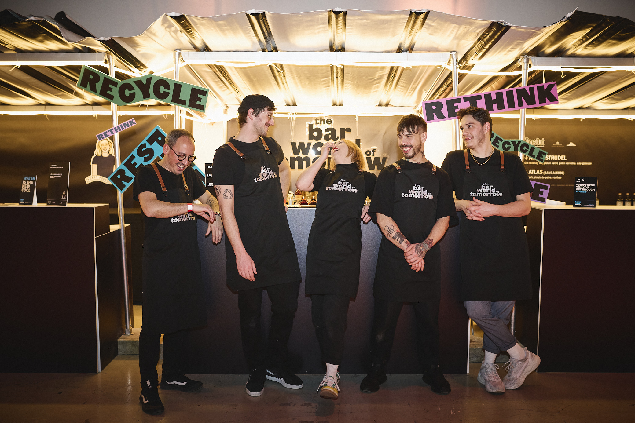 Five staff members wearing black uniforms in front of Bar World of Tomorrow stand