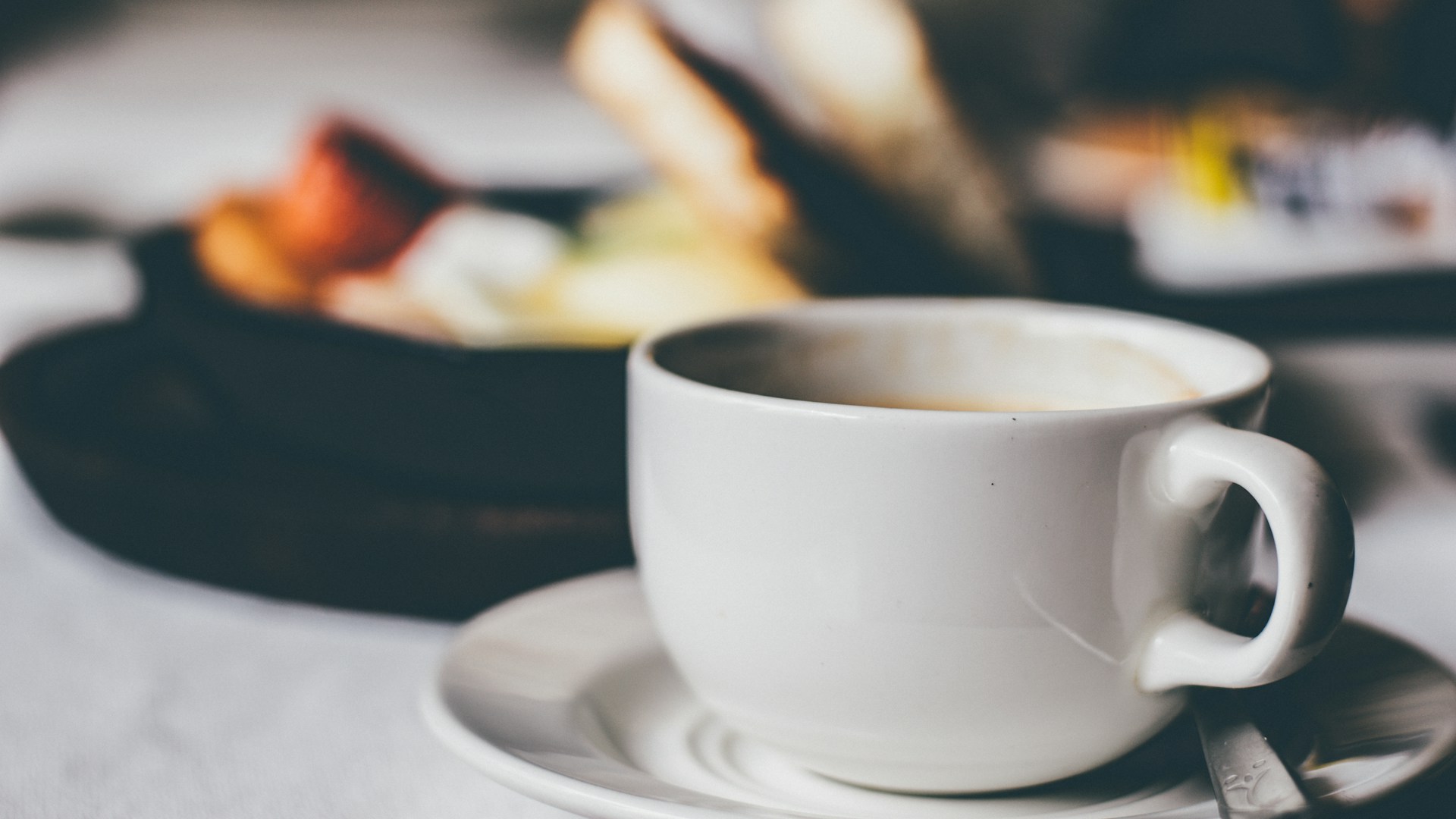 Half empty coffee cup in foreground with food on plates in background