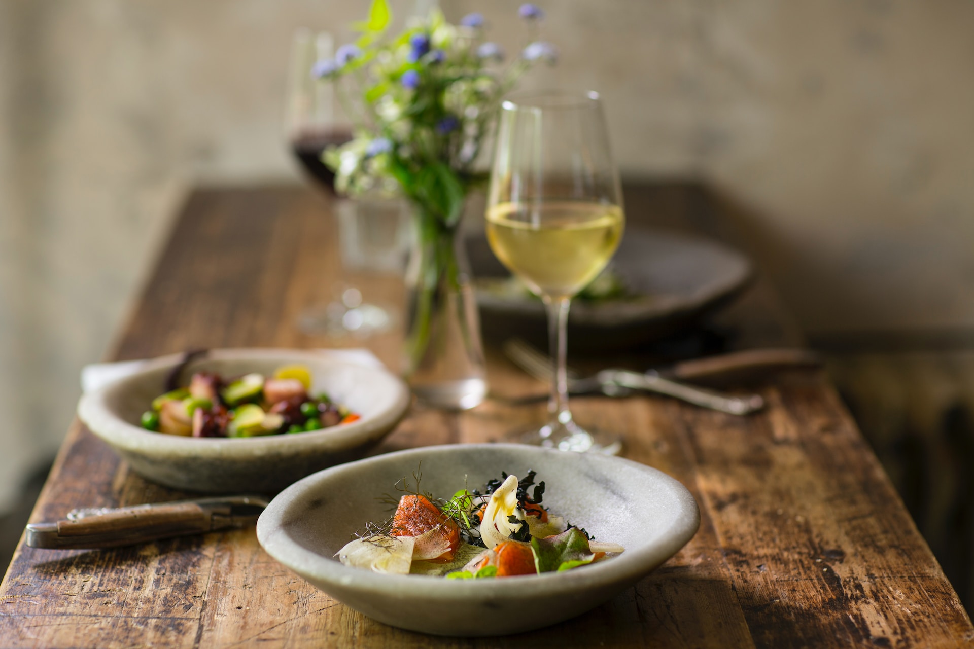 Two grey bowls of elegant salad on wooden table with glass of chilled white wine