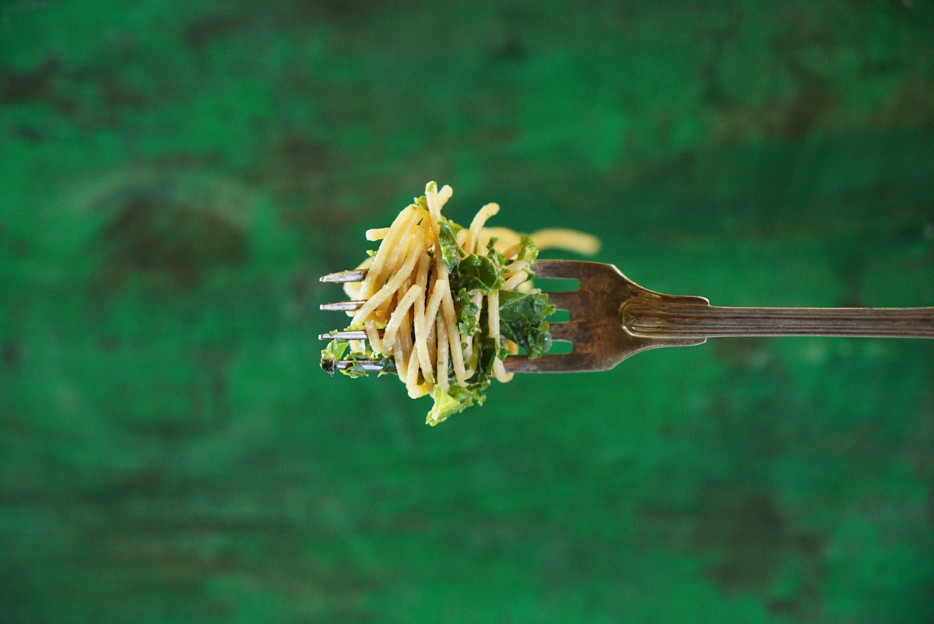 Pasta with herbs on fork held horizontally against green background