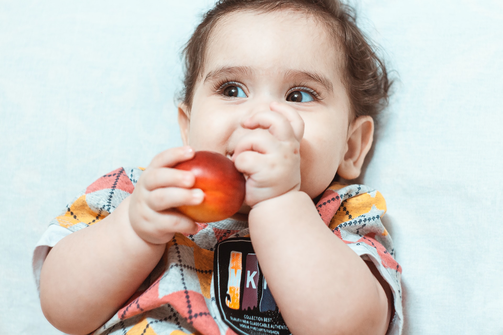 A white toddler smiling and holding an apple