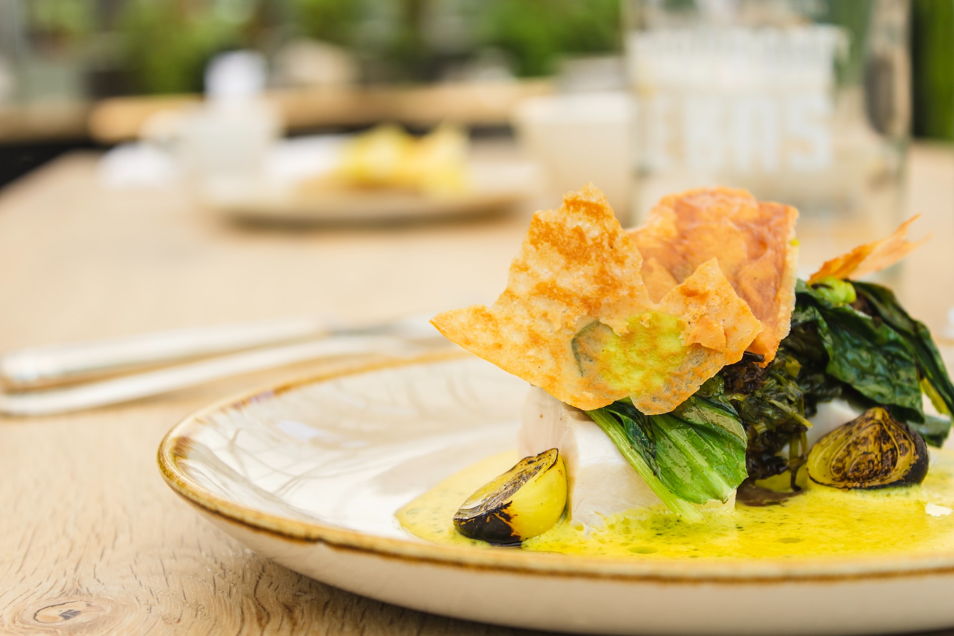 White fish or tofu in bowl with green leafy vegetables and yellow sauce