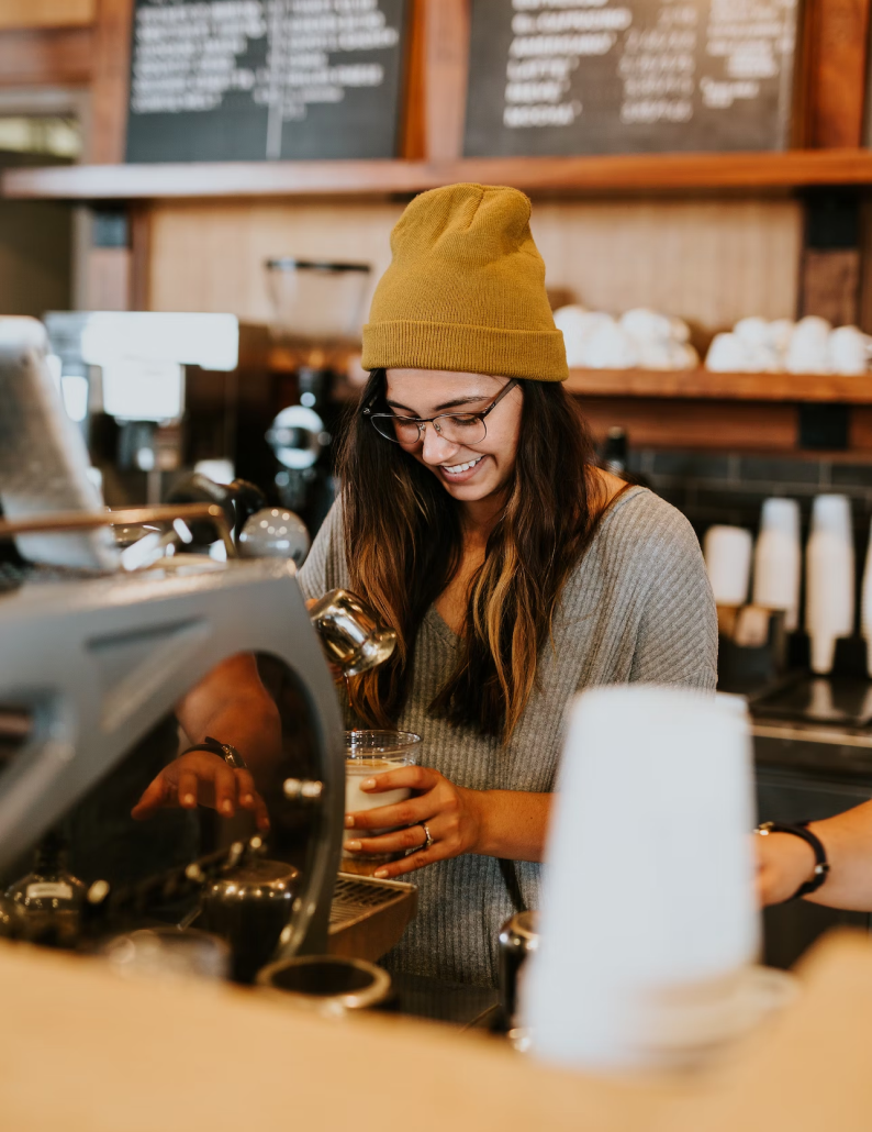 Happy barista in yellow beanie hat making coffee