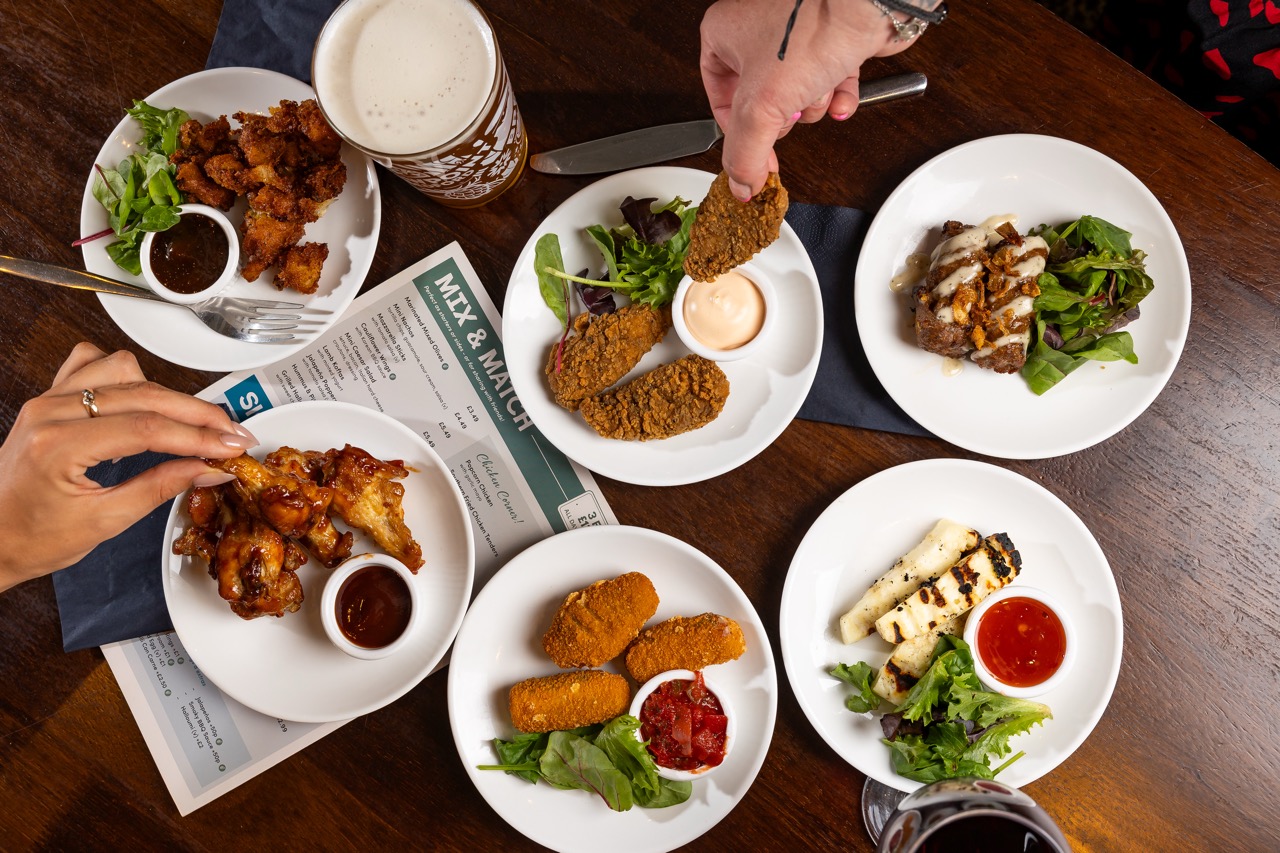 Overhead shot of people sharing small plates of food in a British pub
