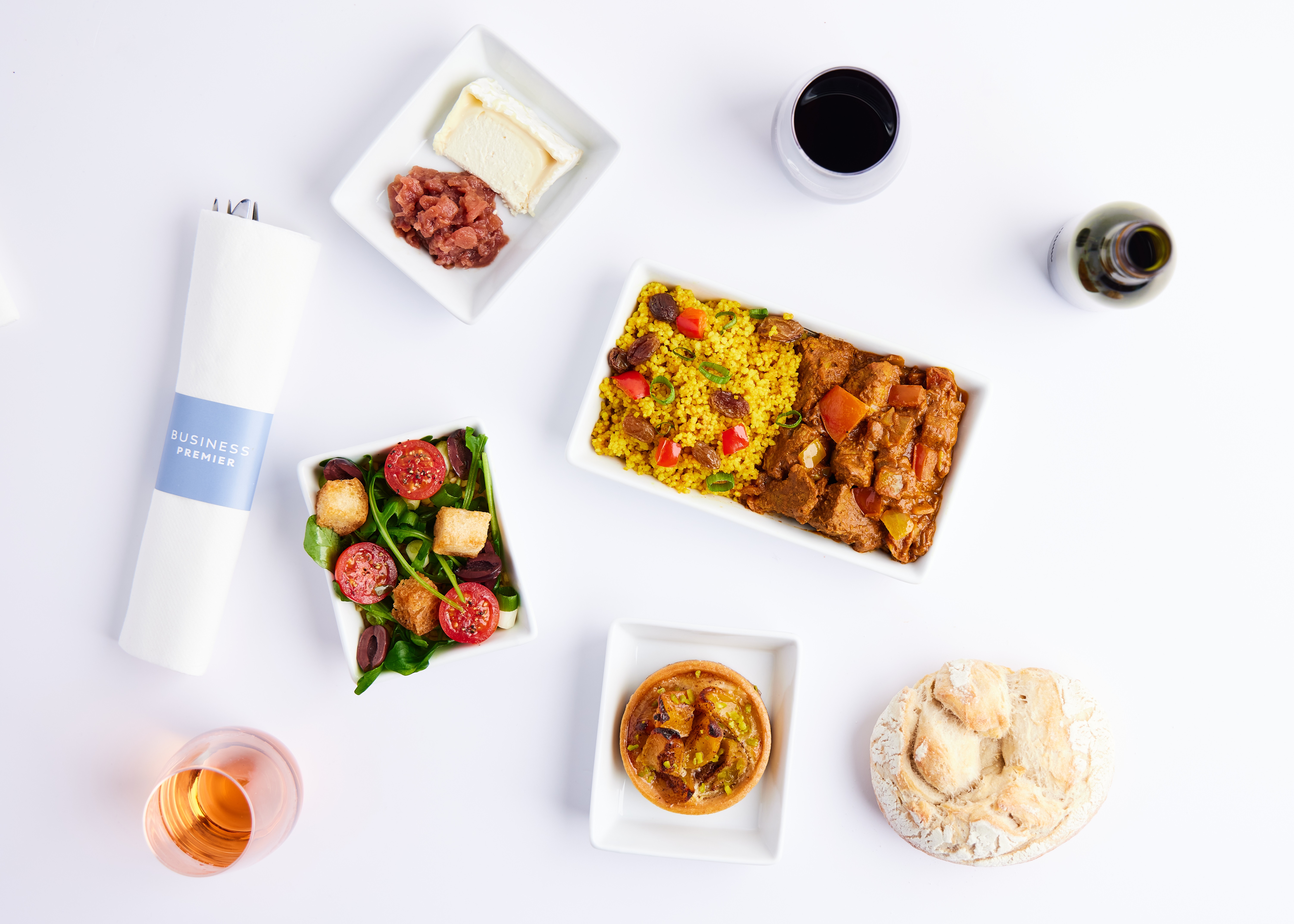 Overhead shot of salads, bread and drinks on white surface with napkin and cutlery