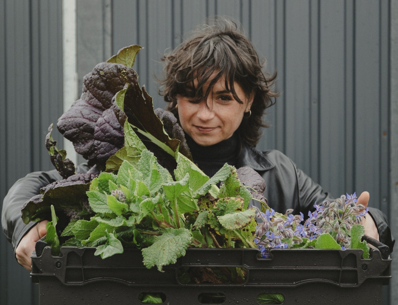 A grower with a box of her produce, smiling at the camera