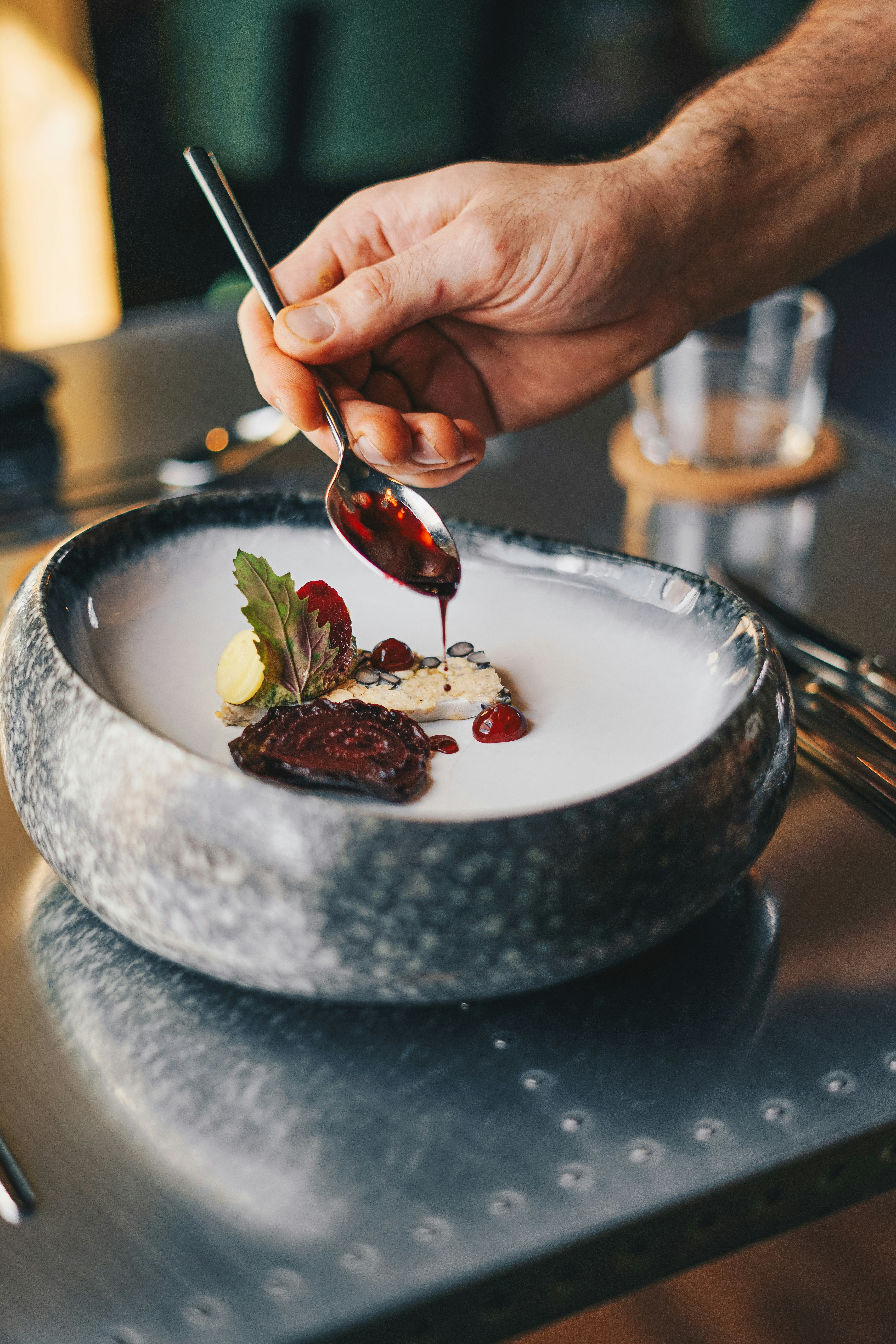 A chef's hand finishing a dish with a drizzle of red syrup from a spoon