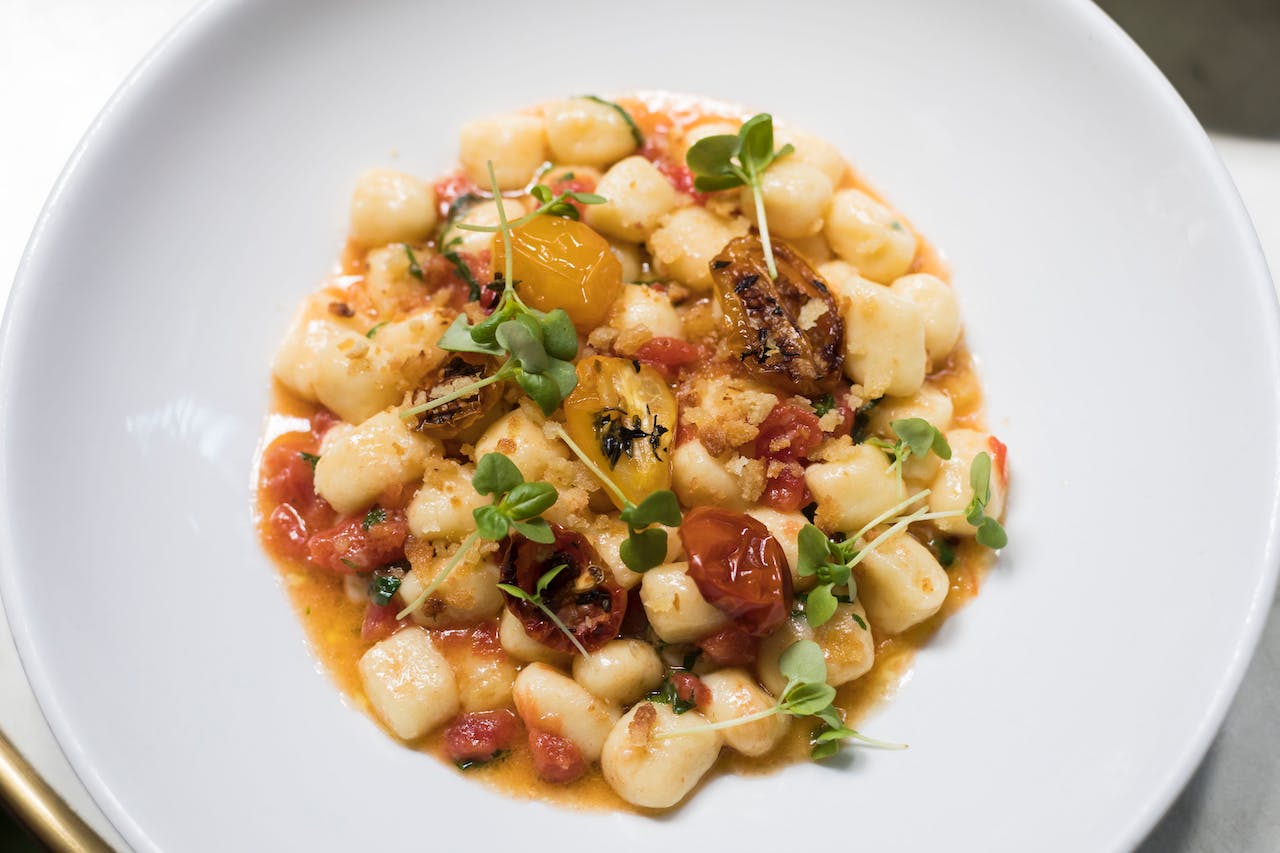 Overhead shot of gnocchi with vegetables and micro-herbs in white bowl