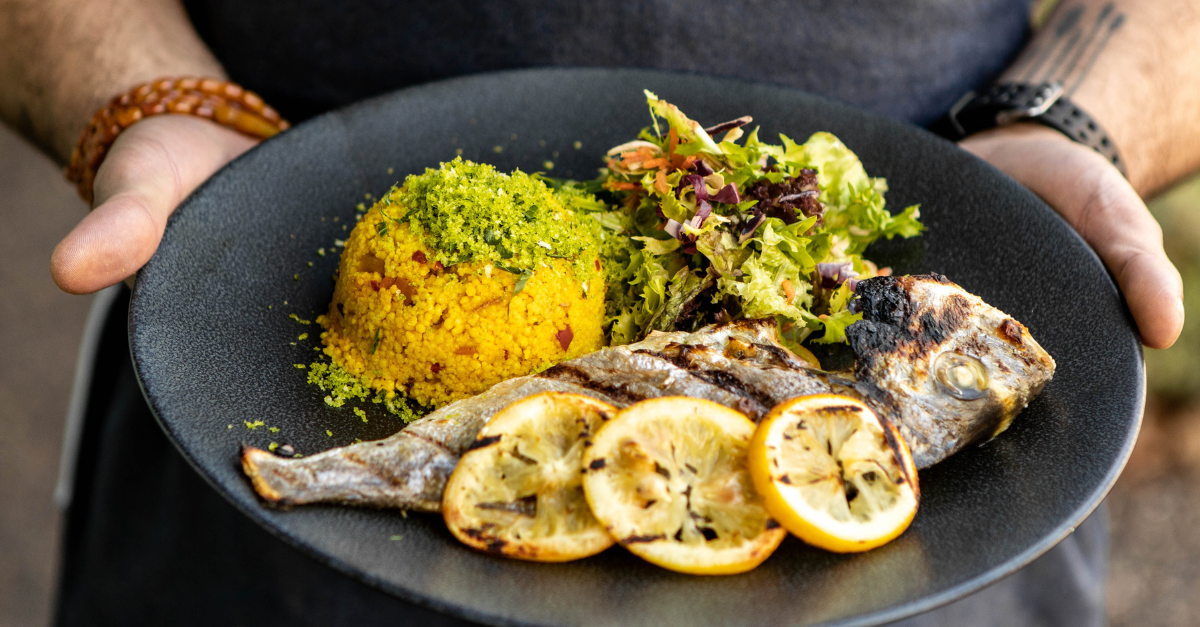 Hands holding plate with whole fish, salad leaves and yellow rice