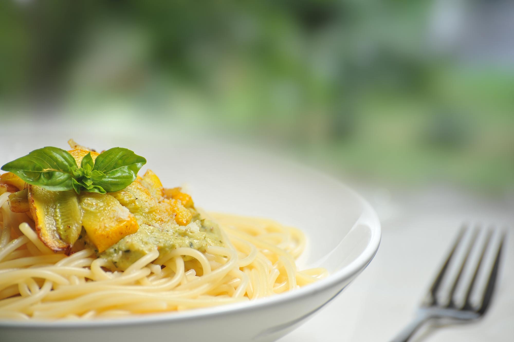 Close up shot of white bowl of spaghetti with yellow courgette, with fork to the right