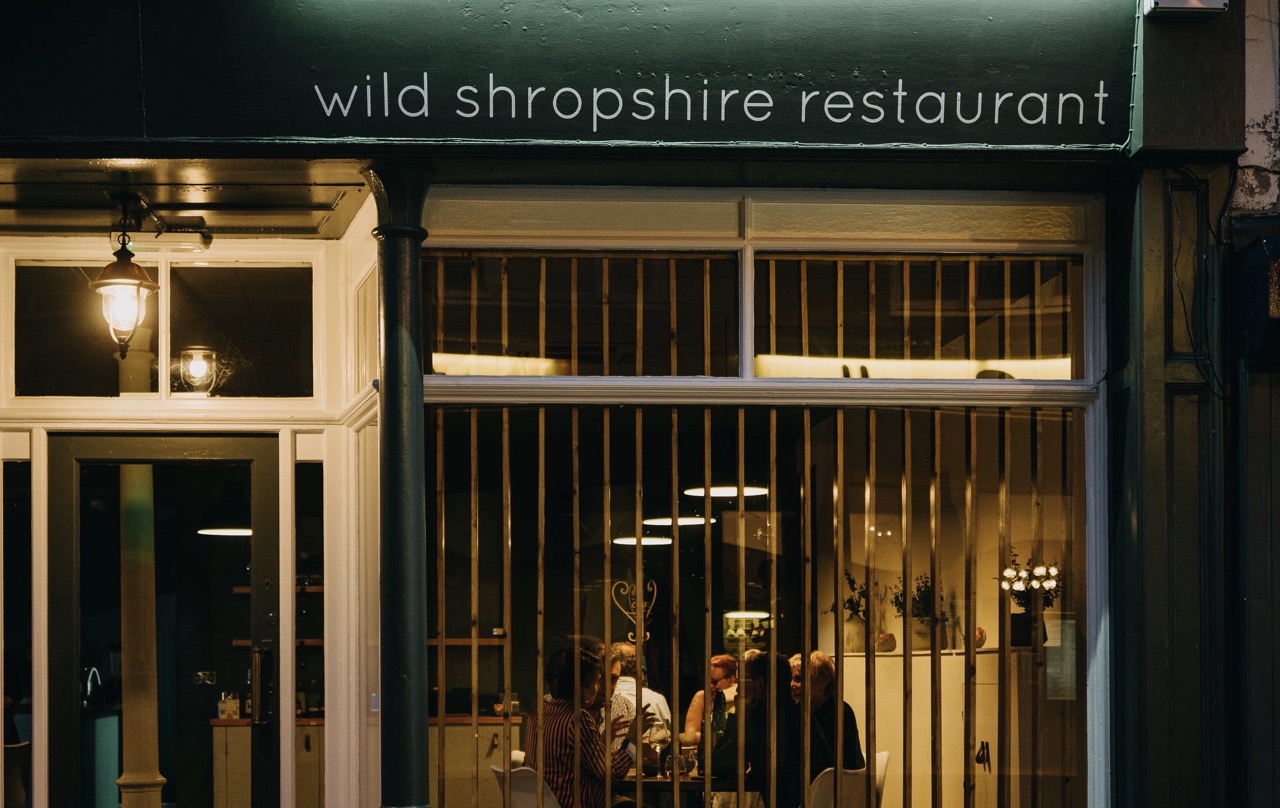 Front of Wild Shropshire restaurant at night, with customers visible through the window