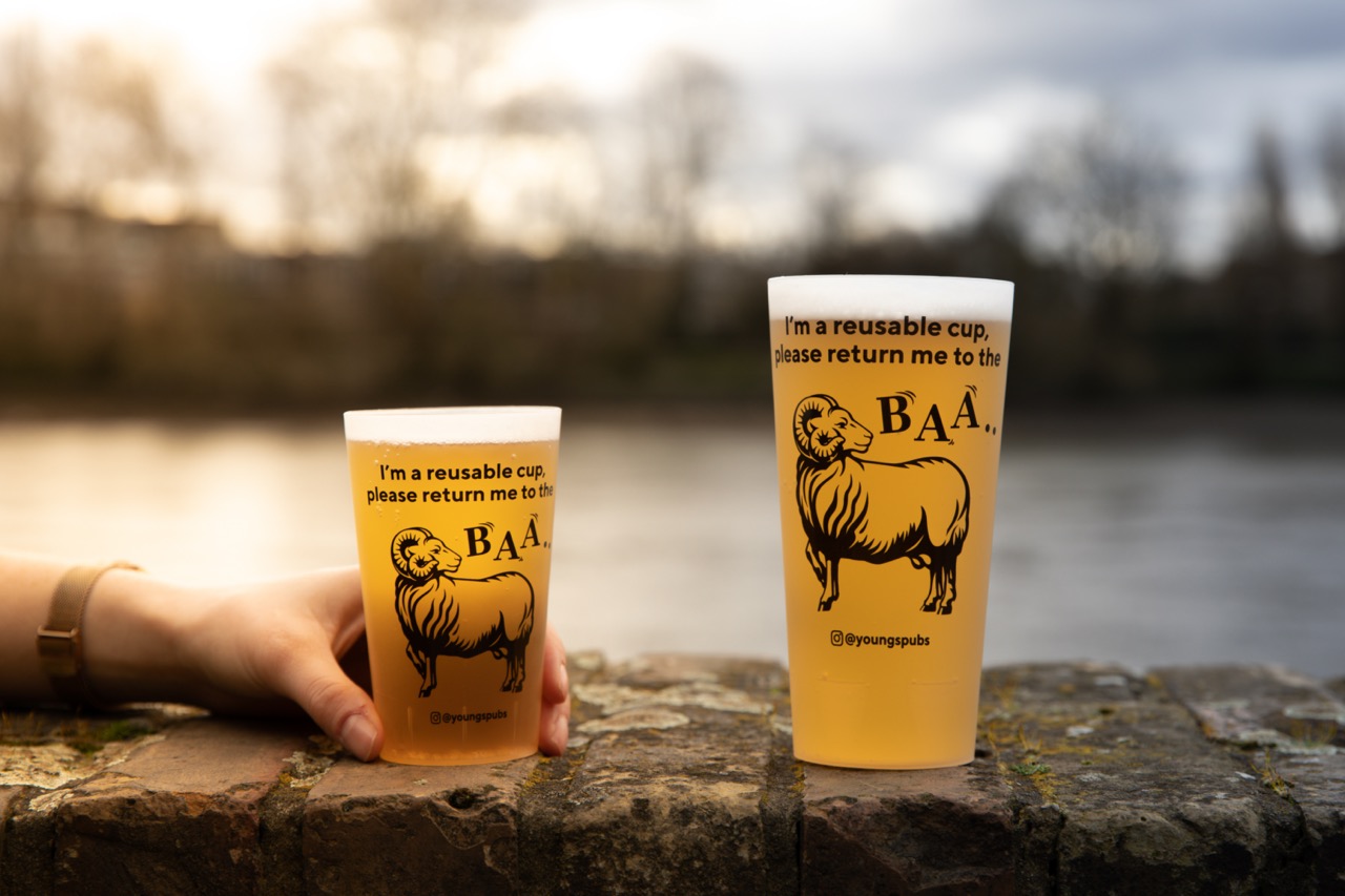 Two reusable plastic cups of beer on an outdoor wall, with a hand reaching into frame to grab one